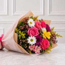 Mixed bouquet of pink, white, yellow, and purple flowers wrapped in paper