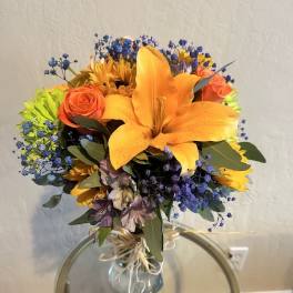 Bouquet of orange lilies, roses, and blue filler flowers in a glass vase