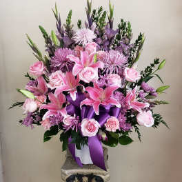 Pink and lavender floral arrangement in a white vase with purple ribbon