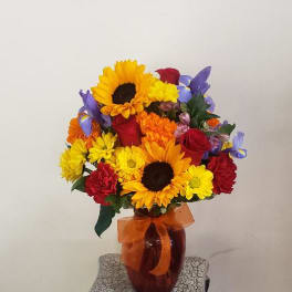 Colorful bouquet in an amber vase with sunflowers, roses, and daisies