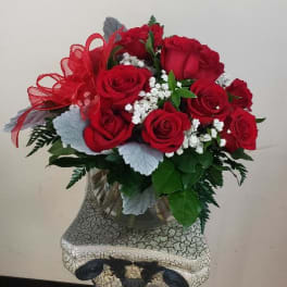 Red roses arranged in a glass vase with a red ribbon bow
