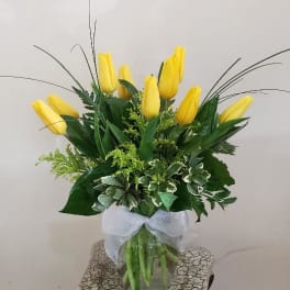 Yellow tulips arranged in a clear glass vase with a white ribbon