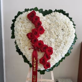 Heart-shaped floral tribute with white flowers and red roses on an easel