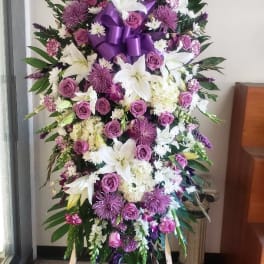 Standing floral spray with white lilies, purple roses, and a purple ribbon