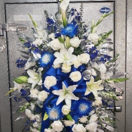Standing floral spray with white lilies, roses, and blue accents on an easel