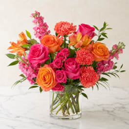 Bouquet of pink and orange roses, carnations, and alstroemeria in a clear glass vase