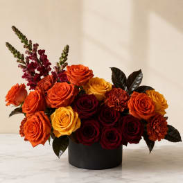 Arrangement of orange, yellow, and burgundy roses in a black vase