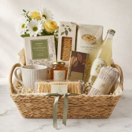 Gift basket with daisies, yellow roses, tea, crackers, soup mix, mug, and a bottle of lemonade