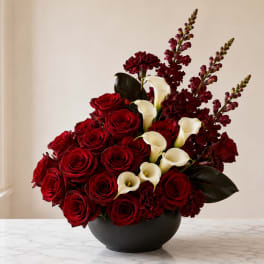 Red roses and white calla lilies arranged in a dark bowl vase