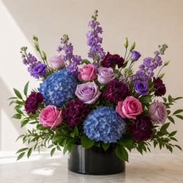 Mixed bouquet of roses, hydrangeas, and purple blooms in a black vase