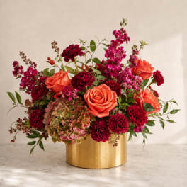 Coral roses and burgundy blooms arranged in a gold vase