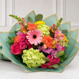 Mixed bouquet of pink, orange, yellow, and green flowers wrapped in teal paper