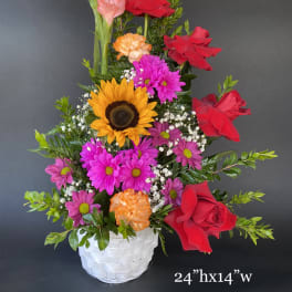 Mixed flower arrangement in a white basket with red roses and sunflowers