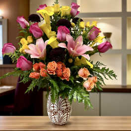 Mixed bouquet of pink roses, yellow callas, and lilies in a patterned vase