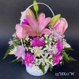 Pink lilies, roses, and daisies arranged in a white basket with a handle