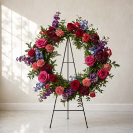 Floral wreath of roses, carnations, and purple blooms on a black stand