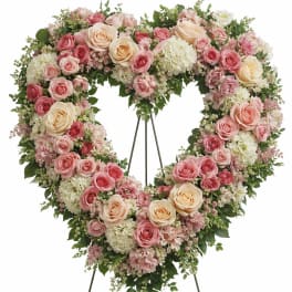 Heart-shaped floral wreath with pink and cream roses on a stand