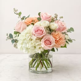 Pink roses, white hydrangea, and peach carnations in a clear glass vase