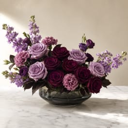 Purple and lavender roses with pink carnations in a glass bowl vase