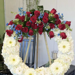 Heart-shaped floral wreath with red roses, white flowers, and blue accents on an easel