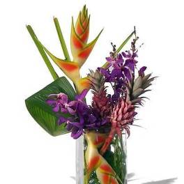 Tropical arrangement with orange and yellow blooms and purple orchids in a clear glass vase