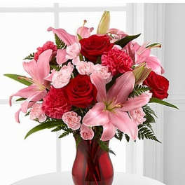 Arrangement of pink lilies, red roses, and pink carnations in a red glass vase