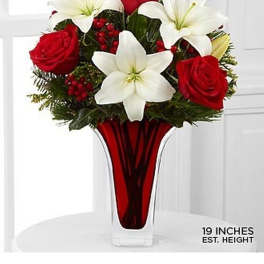 Tall red glass vase with red roses, white lilies, and red berries in a rounded arrangement