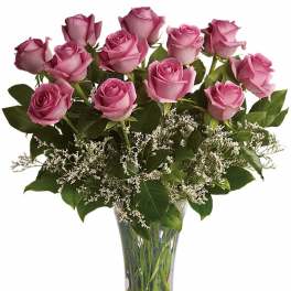 Dozen lavender roses with white filler flowers arranged in a clear glass vase