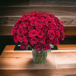 Large bouquet of red roses densely arranged in a clear glass vase on a wooden table