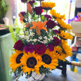 Tiered bouquet with sunflowers, red roses, and orange lilies in a white vase