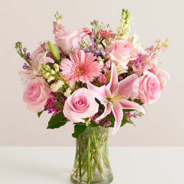 Pink roses, lilies, and mixed blooms arranged in a clear glass vase