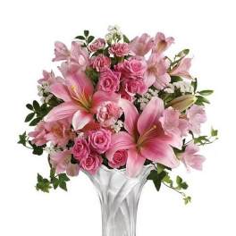 Pink lilies, roses, and carnations arranged in a fluted clear glass vase