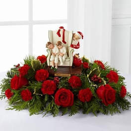 Holiday centerpiece of red roses and carnations with Santa and children figurine in the middle