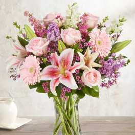 Pink roses, lilies, and gerbera daisies in a clear glass vase