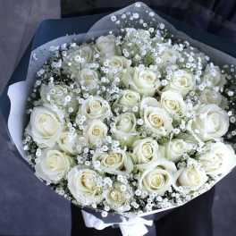 Bouquet of white roses and baby's breath wrapped in dark paper