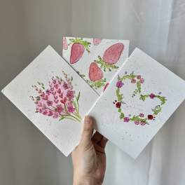 Hand holding three floral watercolor cards with pink designs