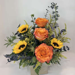 Orange roses and yellow sunflowers in a square vase