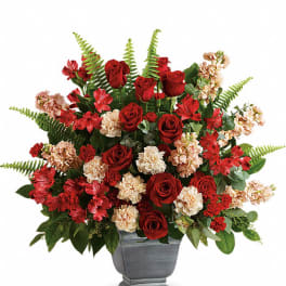 Red roses and peach carnations in a gray urn vase