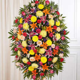 Large standing floral spray with lilies, roses, and daisies in bright mixed colors