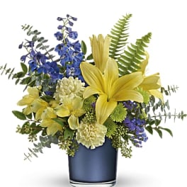 Yellow lilies and blue flowers in a dark glass vase
