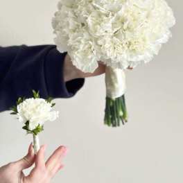 White carnation bouquet and matching boutonniere held against a plain background