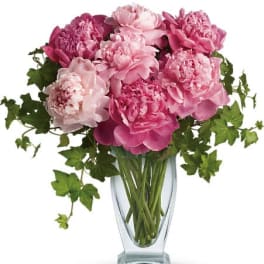 Pink peonies arranged in a clear glass vase with trailing ivy