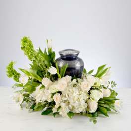 White roses, hydrangeas, and tulips arranged around a dark urn