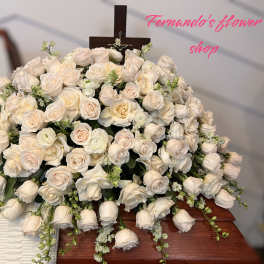 Large spray of ivory roses on a wooden casket with a cross at the back
