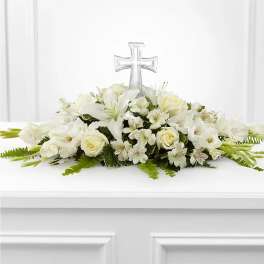 Low white floral spray with lilies and roses accented by a clear cross ornament.
