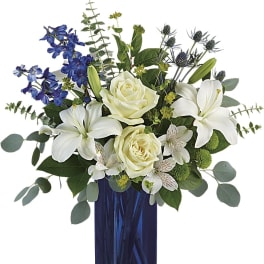 White lilies and cream roses in a blue glass vase with blue flowers