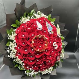 Tightly packed bouquet of red roses with jeweled centers wrapped in black paper with white filler flowers