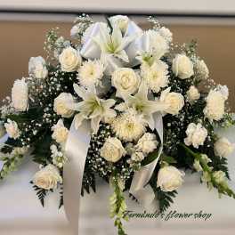 Low white arrangement of lilies, roses, carnations, and mums with a white ribbon bow