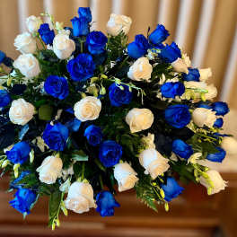 Oval arrangement of blue and white roses with accent flowers in a dense spray.