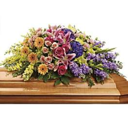 Multicolored casket spray with pink lilies, roses, yellow daisies, and purple flowers on a wooden casket